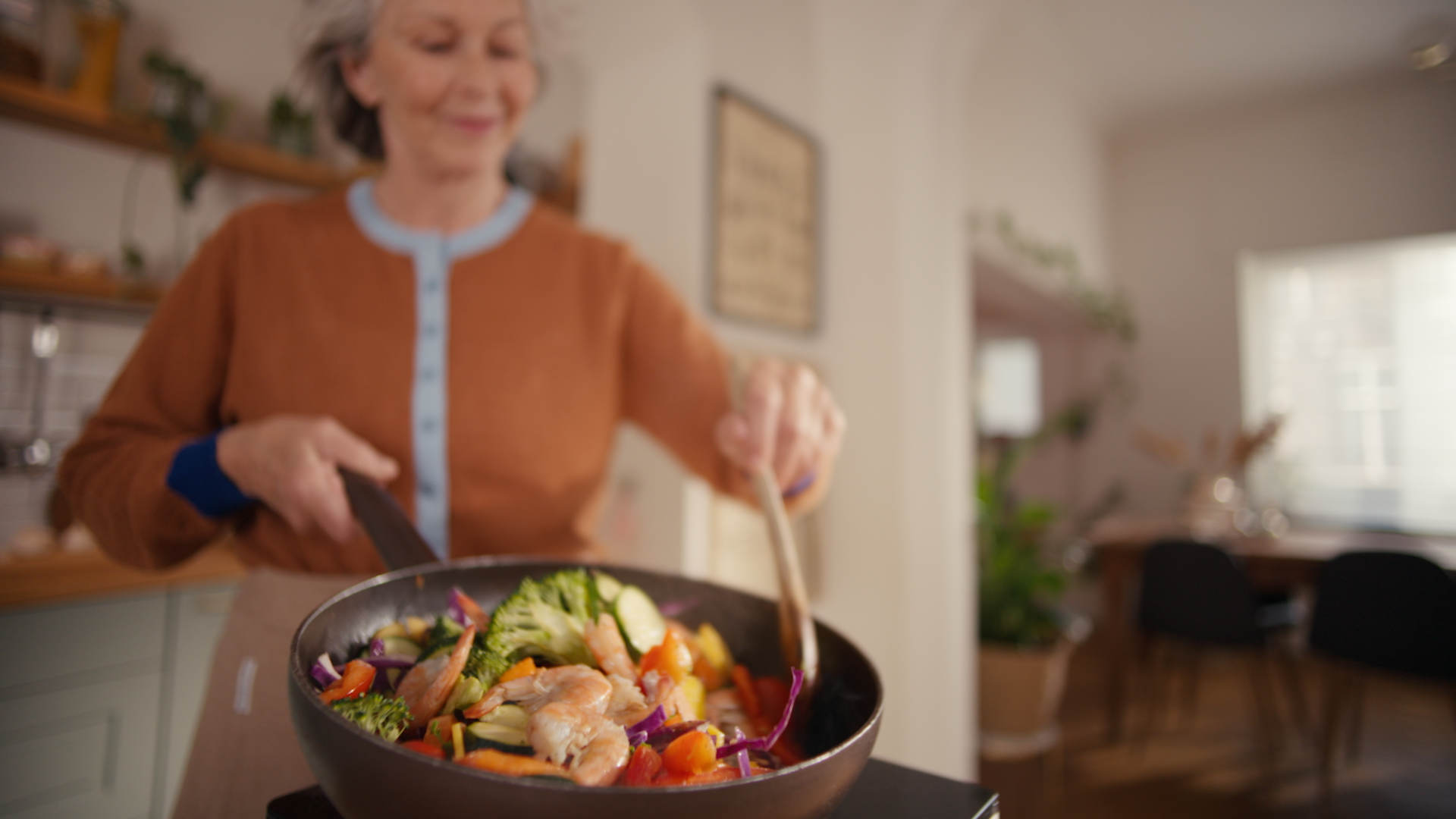 Una donna sorridente che salta in padella un piatto a base di gamberi sprigionandone gli odori in cucina