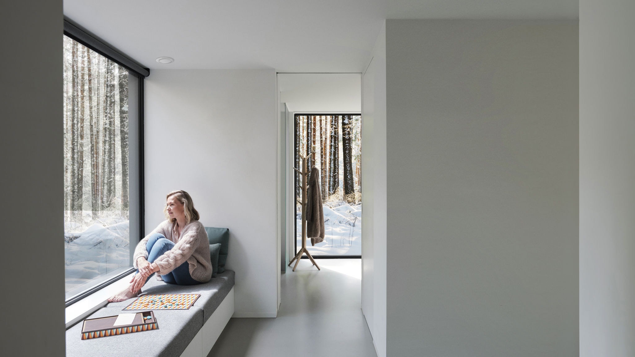 Immagine con una donna a piedi nudi seduta davanti a una finestra mentre guarda gli alberi e la neve all’esterno.