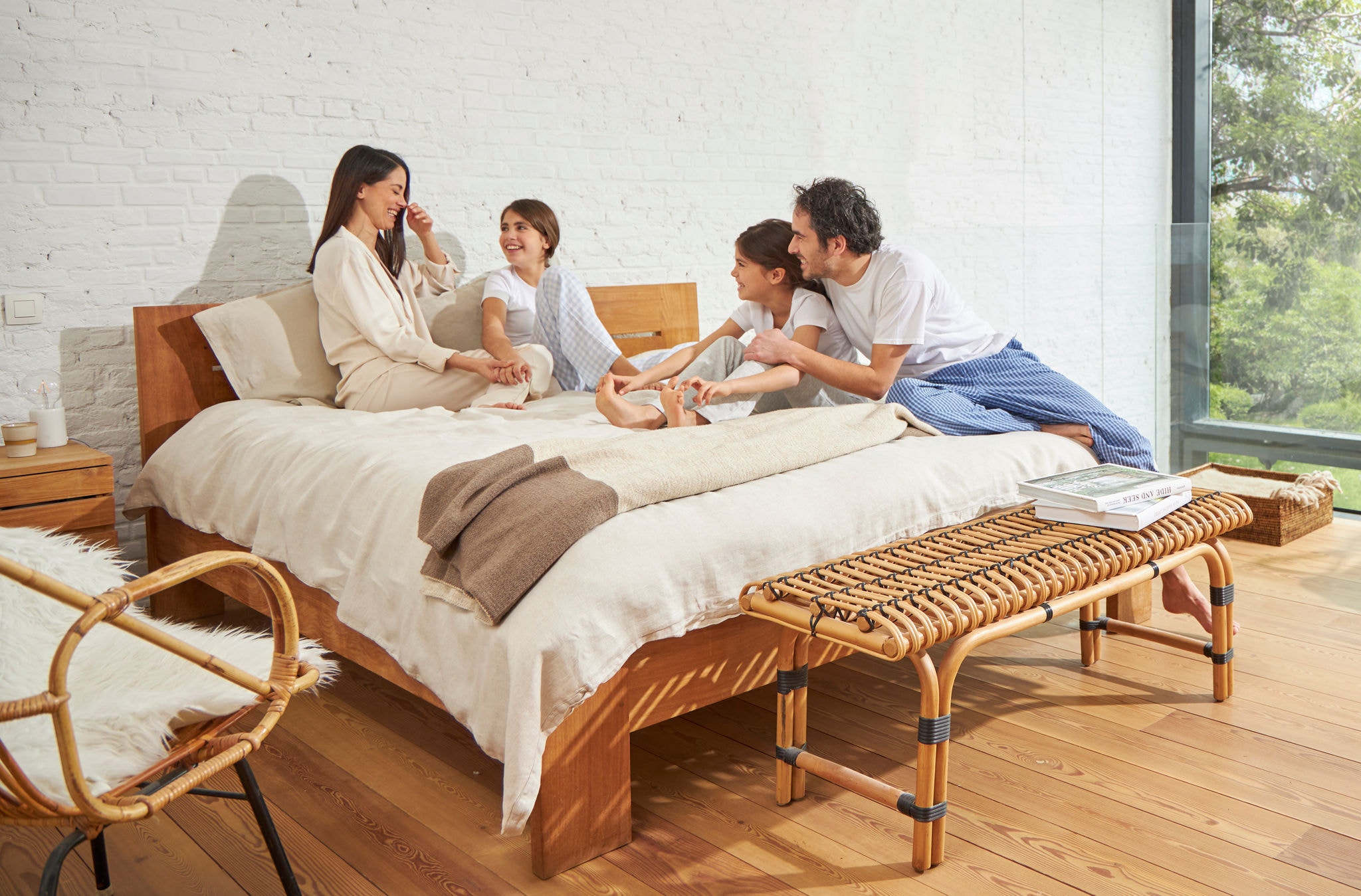 Un uomo e una donna seduti sul letto insieme a due bambine si rilassano, ridono e si godono l’aria pulita.