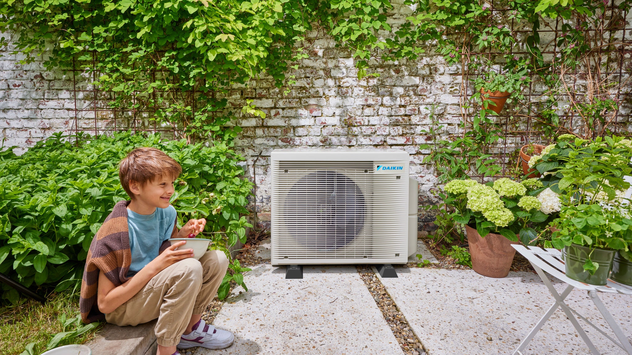 Un bambino sosta vicino a un'unità esterna a pompa di calore ibrida Daikin, che riunisce efficienza energetica e un'estetica piacevole per il giardino