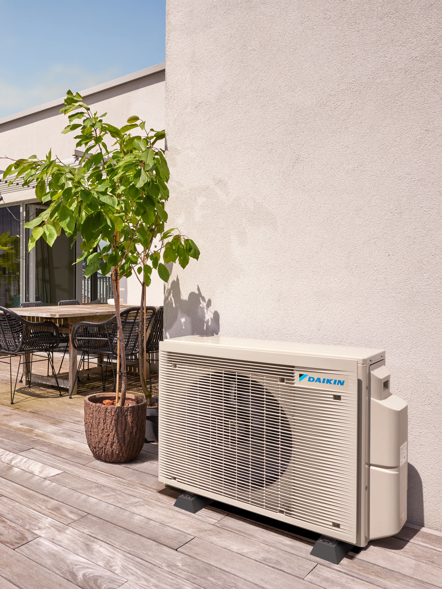 Pompa di calore esterna posizionata in modo discreto contro una parete, ombreggiata da alberi