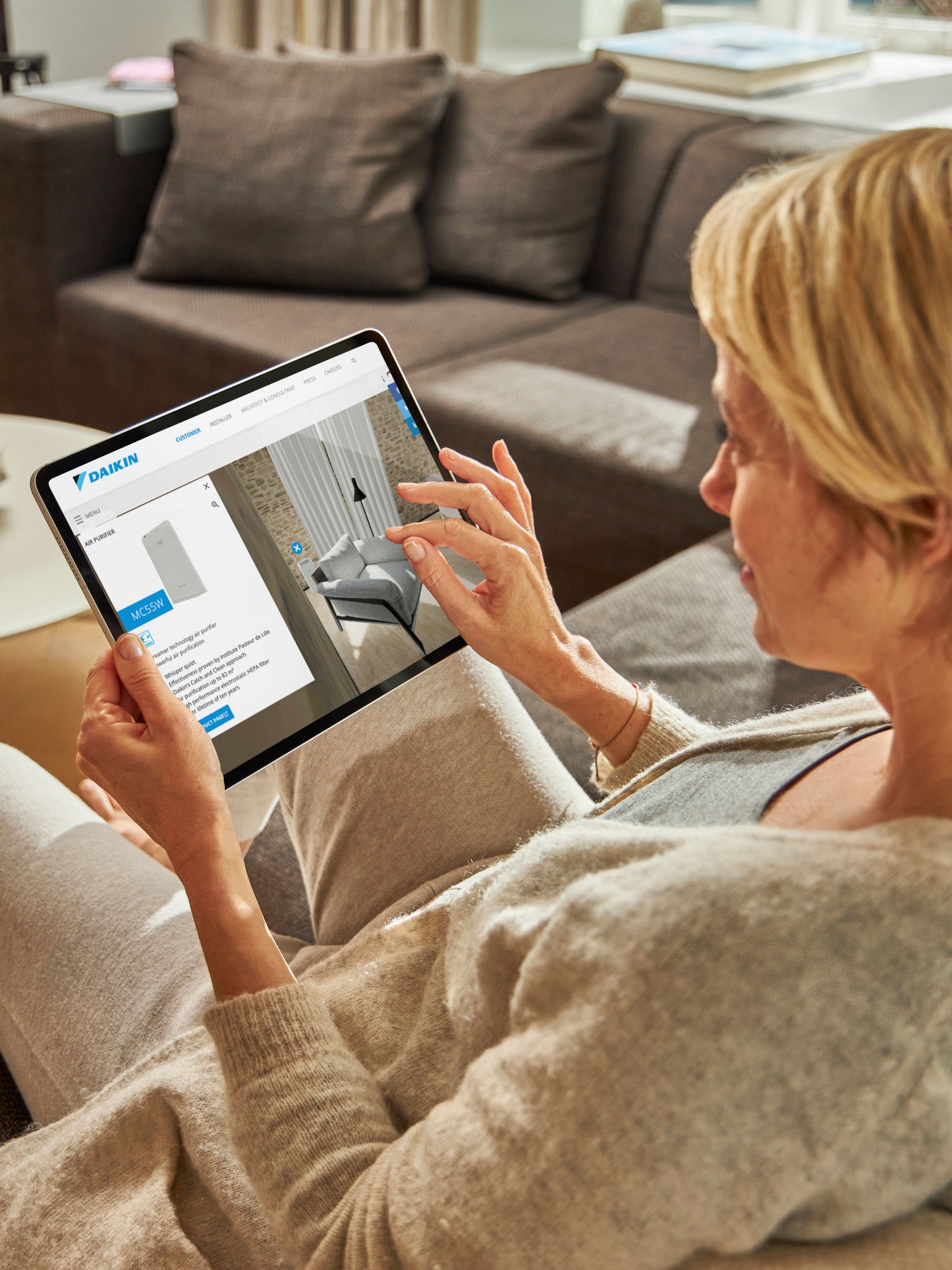Una donna seduta sul divano guarda le pompe di calore aria-acqua nel centro di esperienza virtuale sul suo tablet