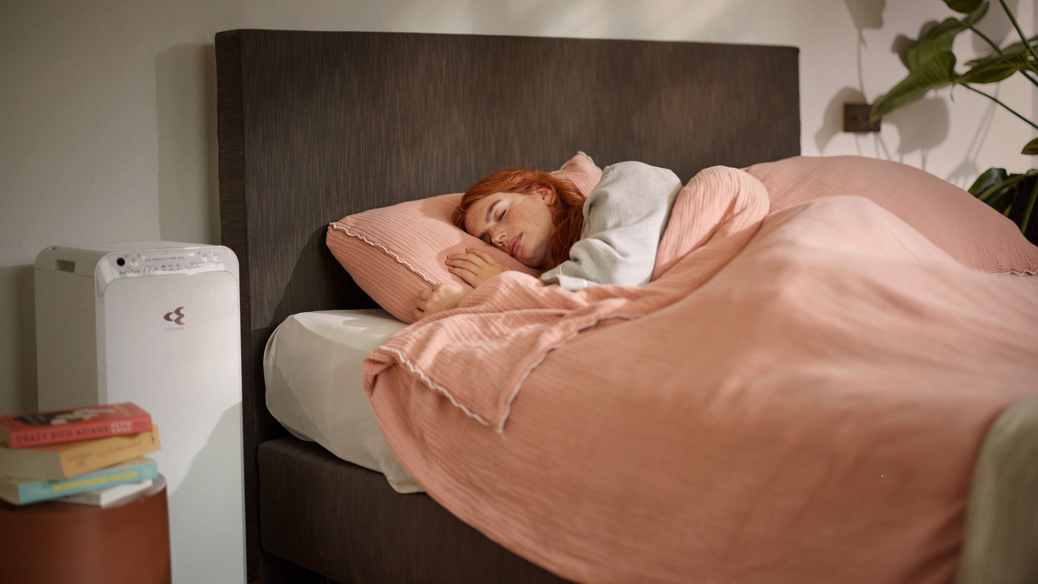Una donna dorme tranquillamente in un letto confortevole, mentre un purificatore d'aria in funzione nelle vicinanze assicura la qualità dell'aria nella camera da letto in inverno