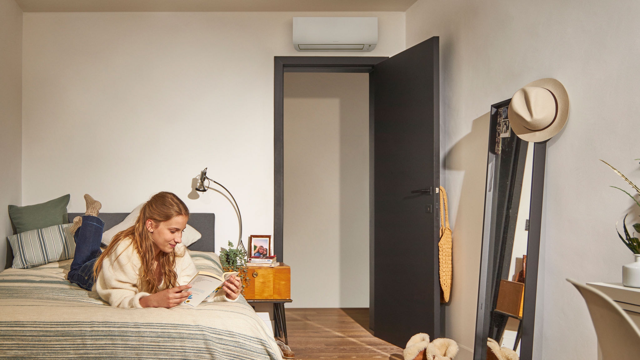 Una donna legge sul letto in un'accogliente camera da letto con un climatizzatore a pompa di calore montato sopra la porta, che assicura un controllo climatico efficiente dal punto di vista energetico