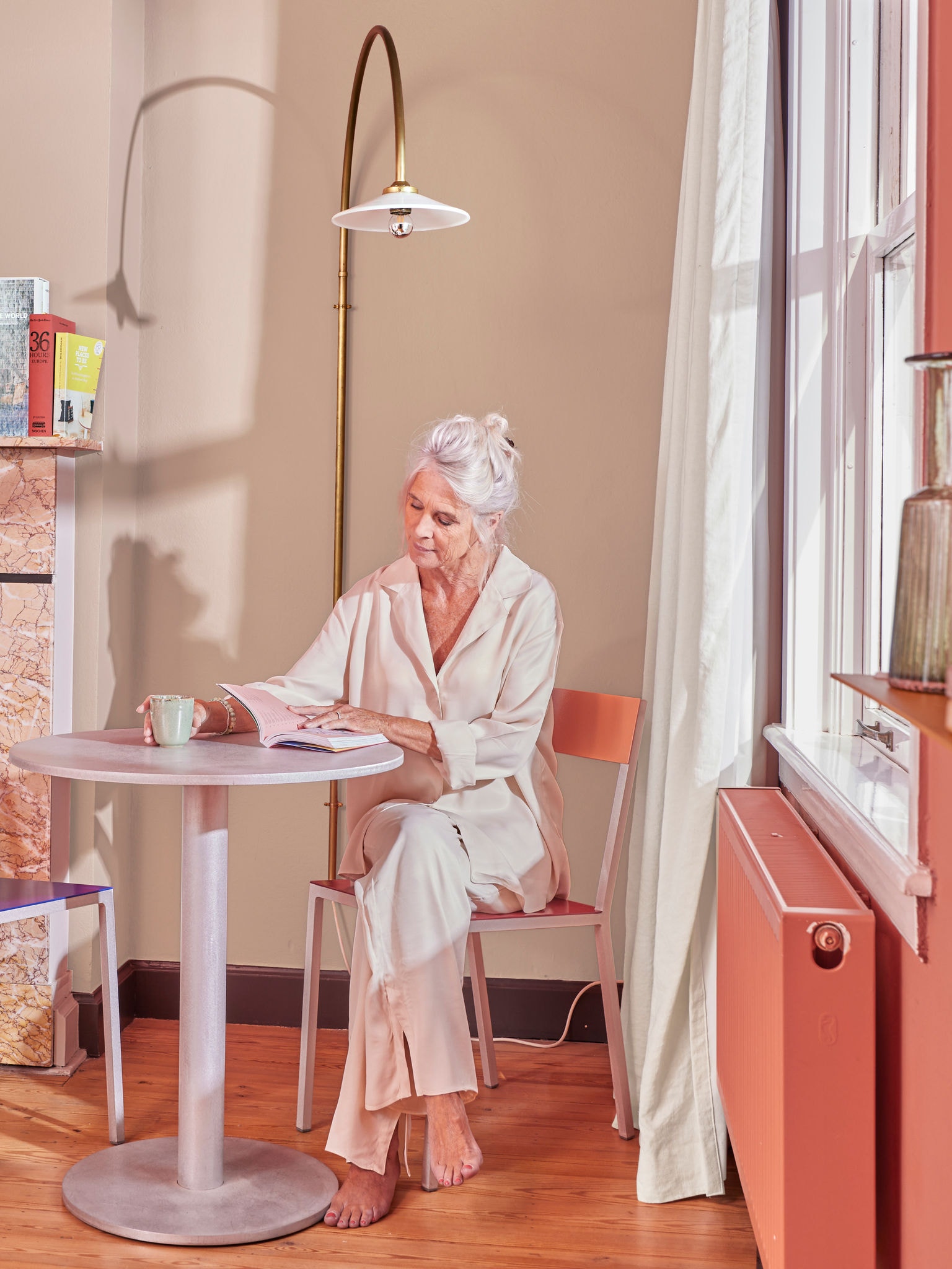 Donna che legge al tavolo vicino a un termosifone collegato a un impianto di riscaldamento domestico con pompa di calore