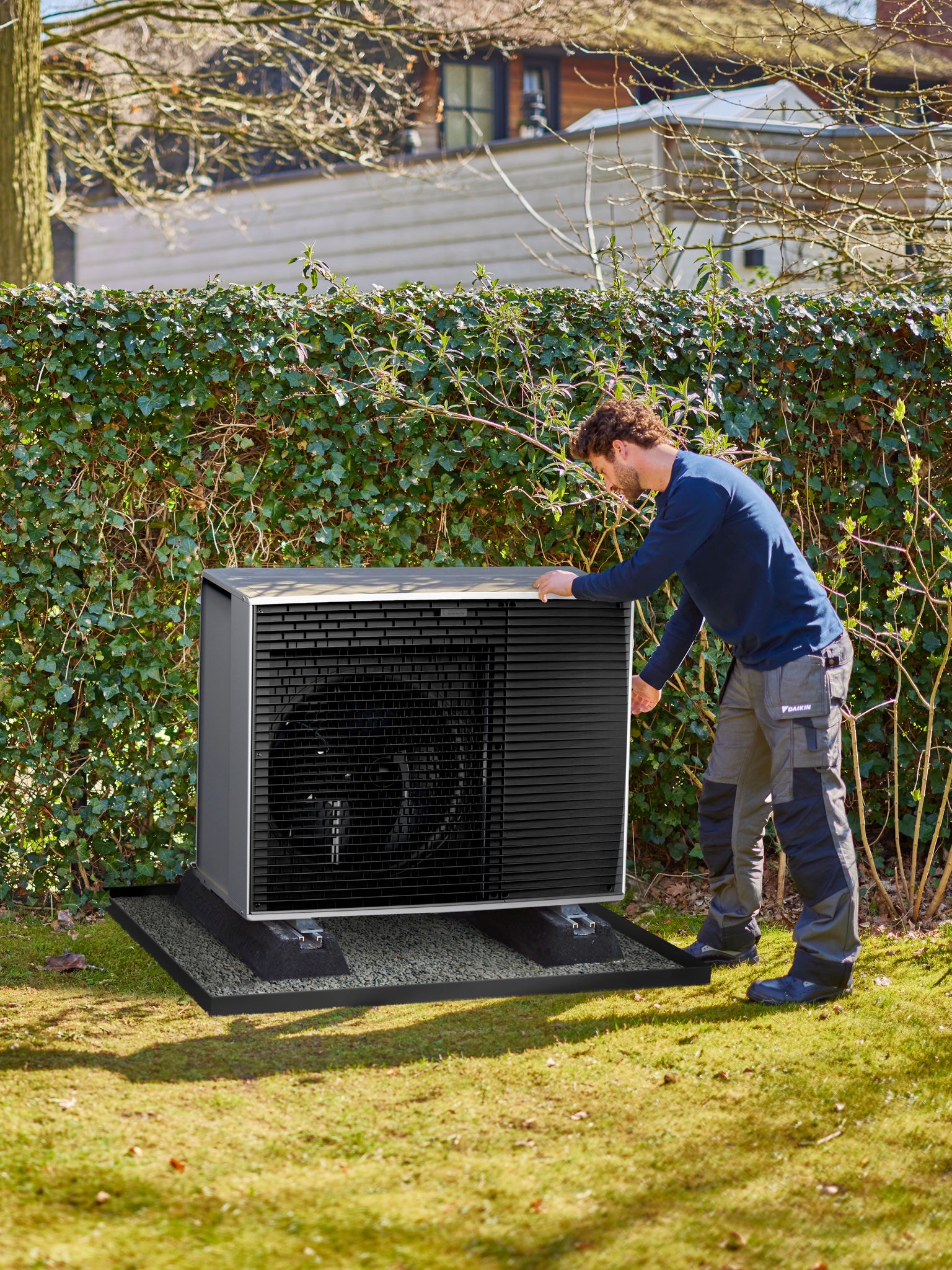 Un installatore colloca una pompa di calore in un punto discreto del giardino, accanto a una siepe