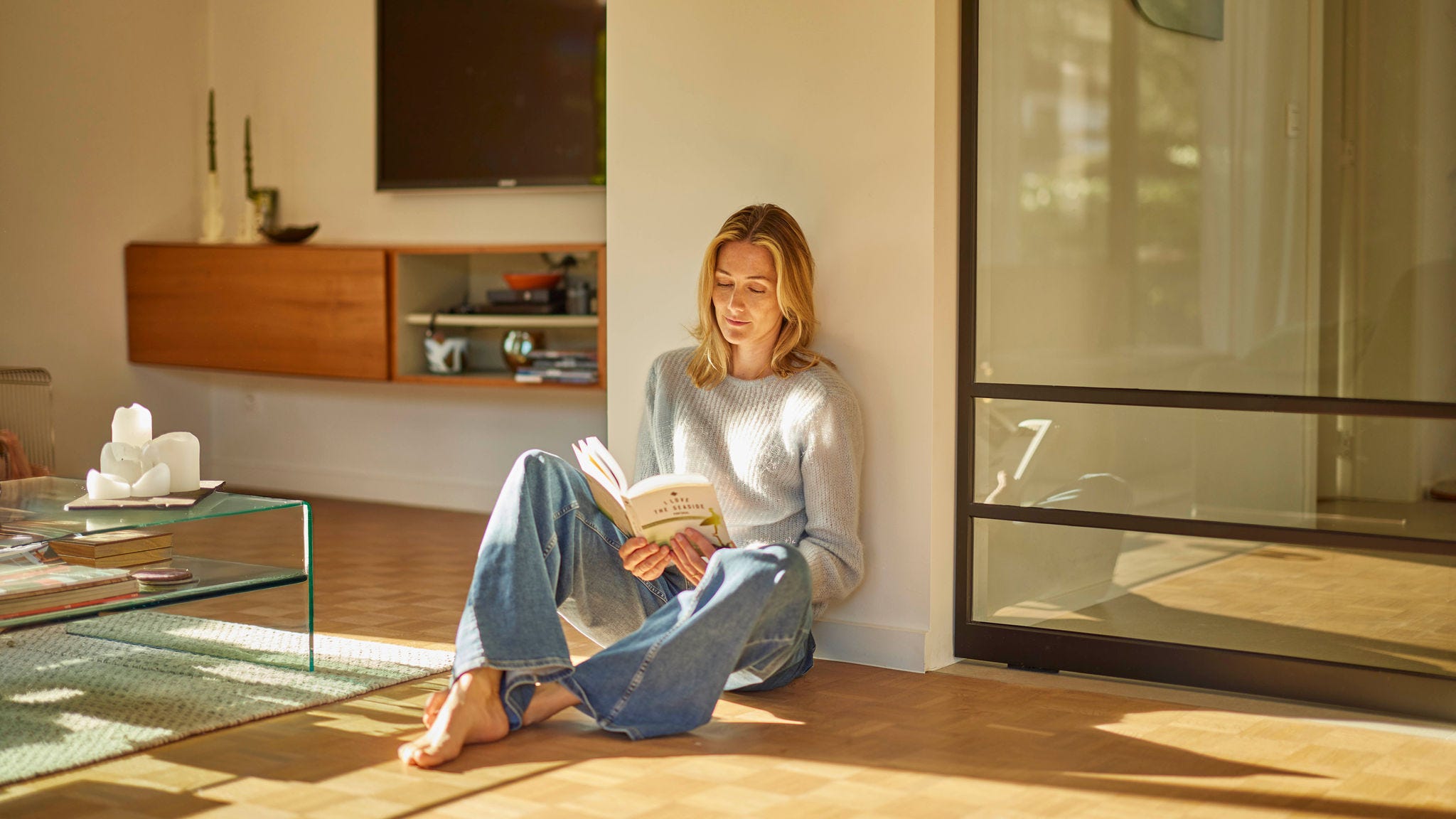 Una donna seduta a leggere su un pavimento di legno con riscaldamento a pavimento in un ambiente perfettamente riscaldato