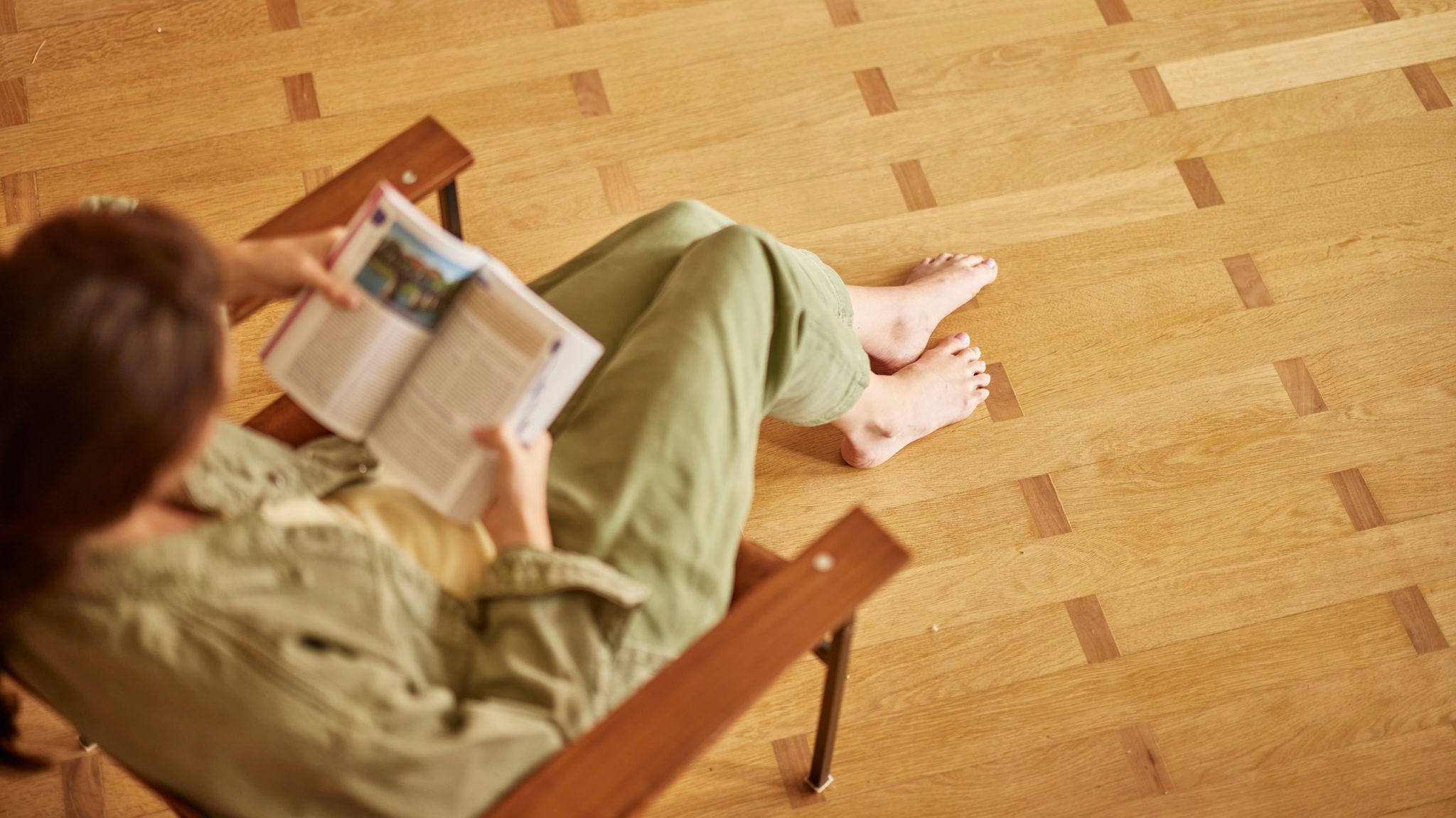 Una donna scalza seduta su un pavimento in legno si gode il comfort del riscaldamento a pavimento mentre legge un libro