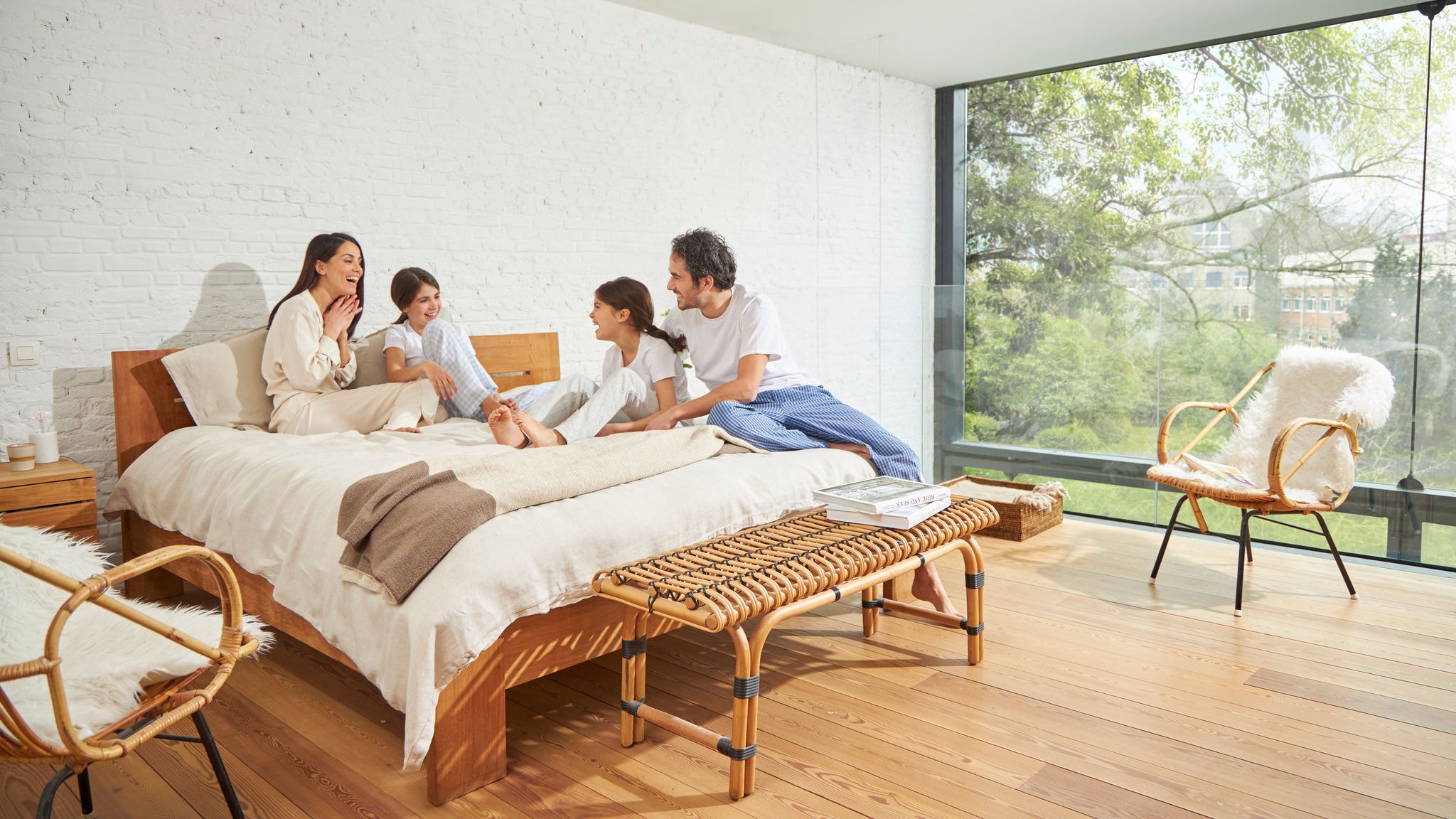Una famiglia che conversa sul letto in una camera con un'ampia parete vetrata, dove la qualità dell'aria interna è ottima e la luce naturale è abbondante