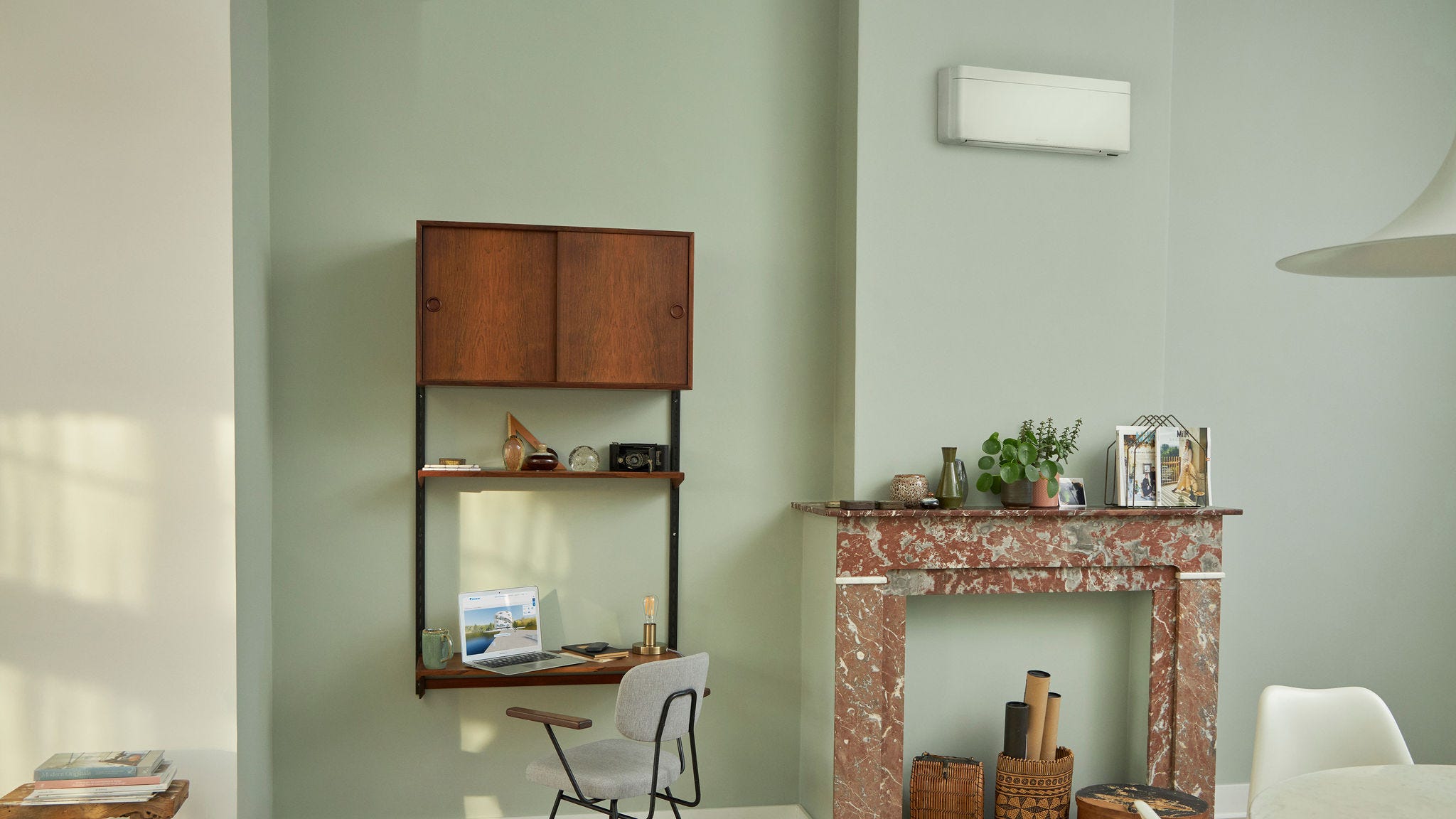 Una pompa di calore a parete dal design minimalista installata in una stanza dalle pareti verde salvia sopra una mensola decorativa