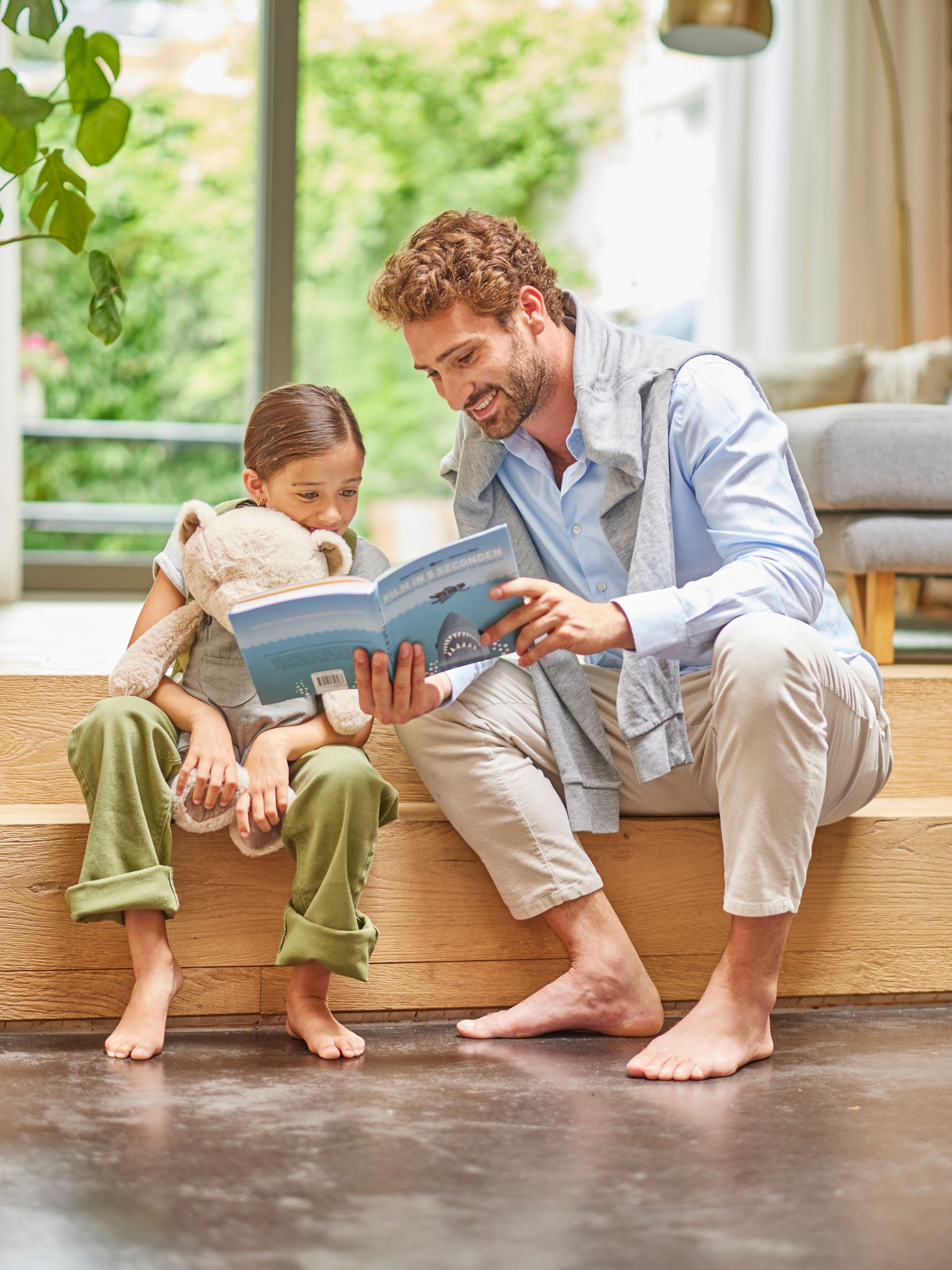 Un papà legge un libro a suo figlio, mentre siedono entrambi scalzi sul pavimento